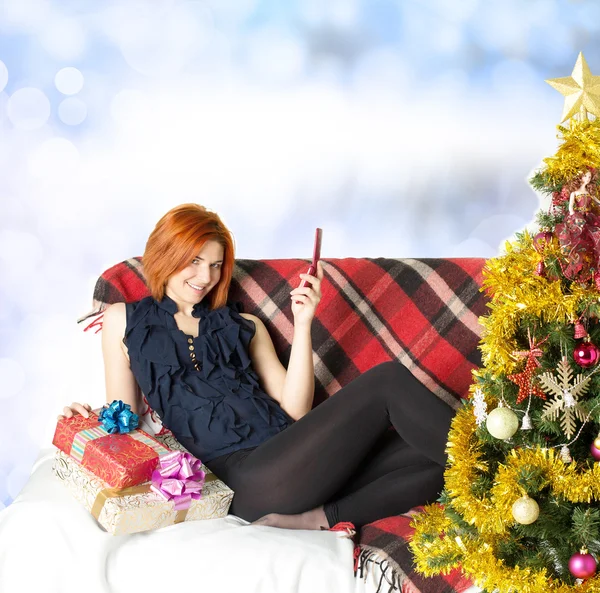 Menina feliz no sofá com um telefone e uma caixa de presente — Fotografia de Stock