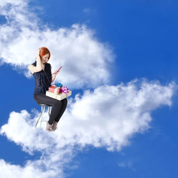 Heureuse fille aux cheveux roux avec des cadeaux et un téléphone dans les rêves de nuages sur une chaise — Photo