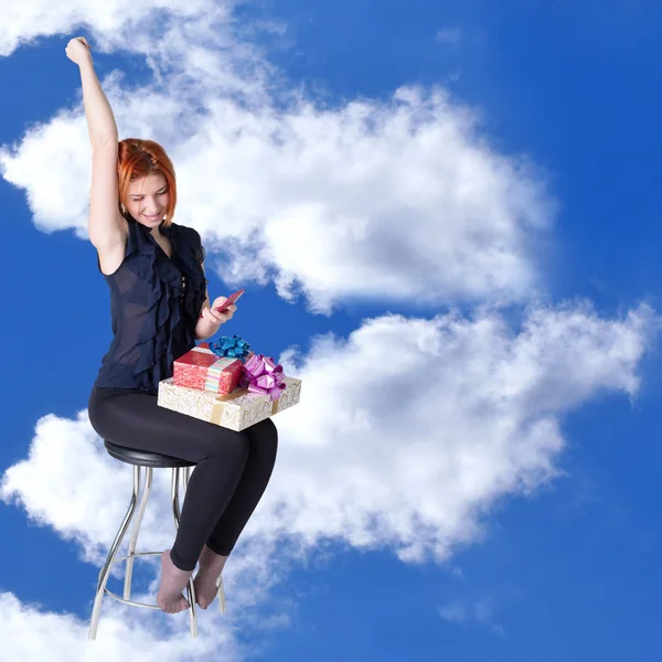 Chica pelirroja feliz con regalos y un teléfono en la nube sueña en una silla — Foto de Stock