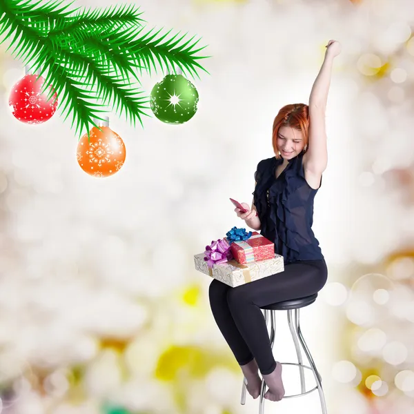 Glückliche rothaarige Mädchen mit Geschenken und Telefon auf einem Stuhl. Weihnachten und Neujahr — Stockfoto