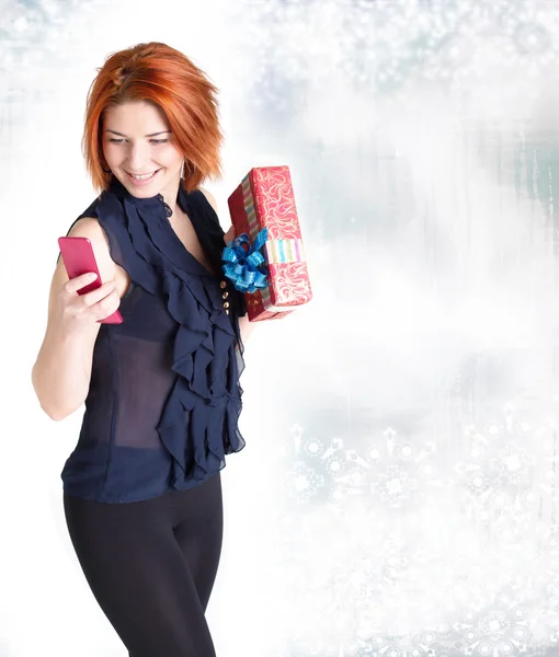 Счастливая девушка с телефоном и подарком на абстрактном рождественском фоне — стоковое фото