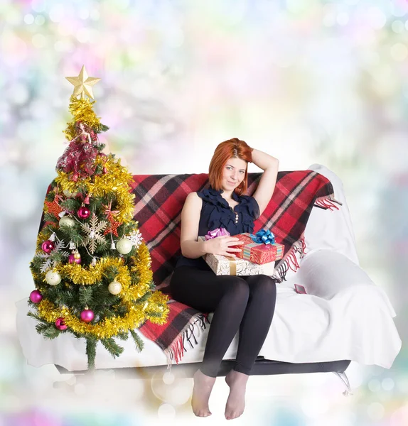 Chica feliz en el sofá con un teléfono y una caja de regalo en las vacaciones de Navidad — Foto de Stock