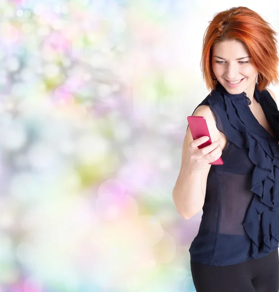 Эмоциональная девушка с рыжими волосами и телефоном на абстрактном праздничном фоне — стоковое фото