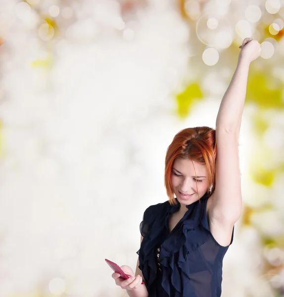 Emotionele gelukkig vrouw met rood haar en een telefoon op de abstracte feestelijke achtergrond — Stockfoto