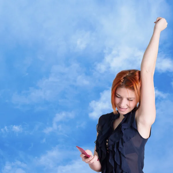 Connect.Happy roodharige meisje met mobiele telefoon op een blauwe hemelachtergrond. — Stockfoto