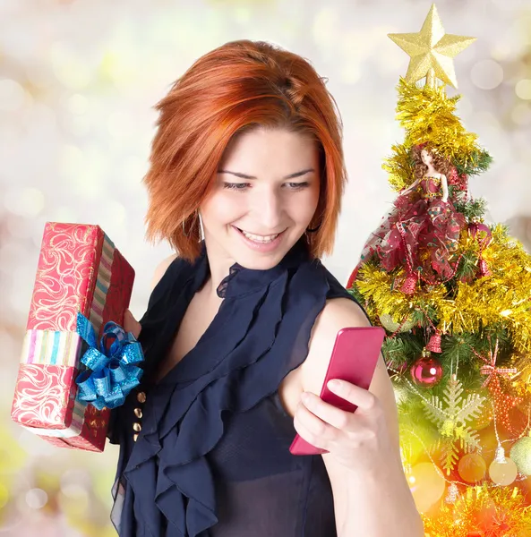 Felice donna dai capelli rossi sorridente con scatole regali e telefono all'albero di Natale. Concetto vacanza — Foto Stock