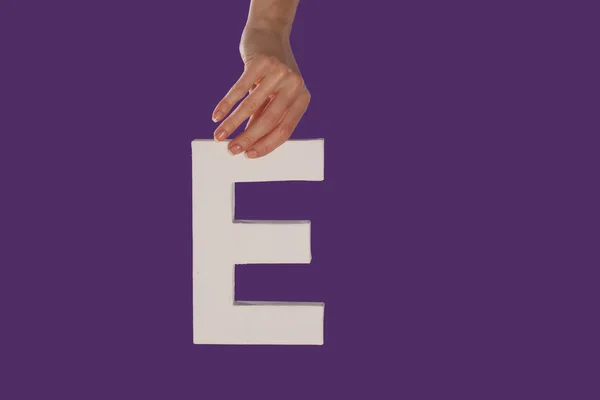 Mano femenina sosteniendo la letra E desde arriba — Foto de Stock