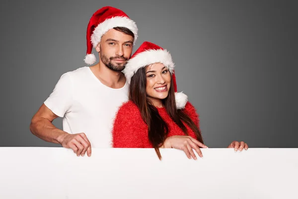 Coppia che indossa cappelli Babbo Natale in possesso di una tavola vuota — Foto Stock