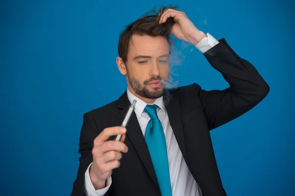 Бизнесмен с электронной сигаретой в костюме и галстуке на синем — стоковое фото