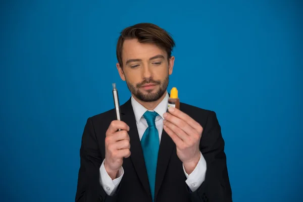 Geschäftsmann hält E-Zigarette und E-Liquid auf blau — Stockfoto