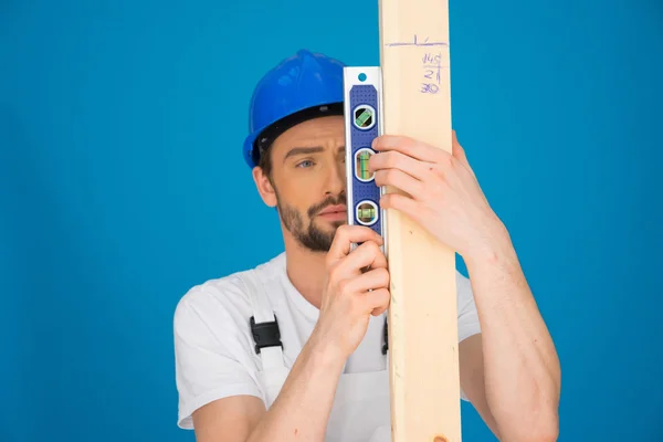 Builder holding a spirit level and plank of wood — Stock Photo, Image