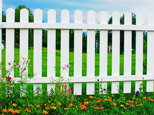 White fence on green grass with flowers.