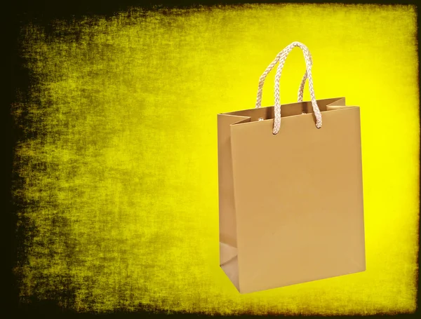 Saco de compras dourado em um fundo grungy amarelo . — Fotografia de Stock