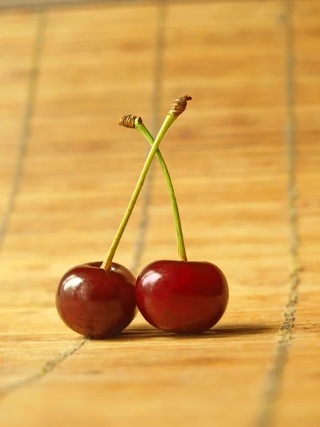 Dos cerezas maduras en la superficie de bambú . — Foto de Stock