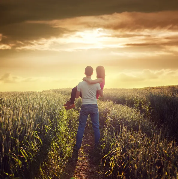 L'homme porte une femme au champ d'été au coucher du soleil — Photo