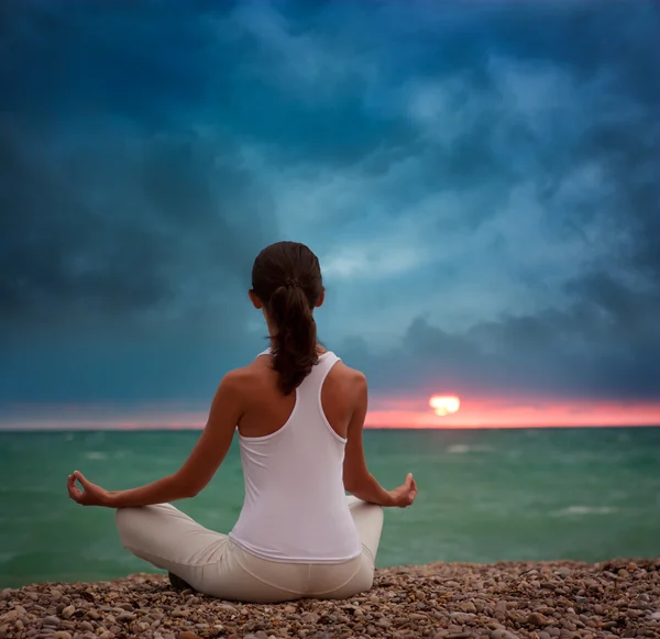 Žena cvičení jógy u moře při západu slunce — Stock fotografie