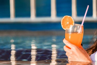 Kadın eli yüzme havuzunda kokteyl tutuyor.