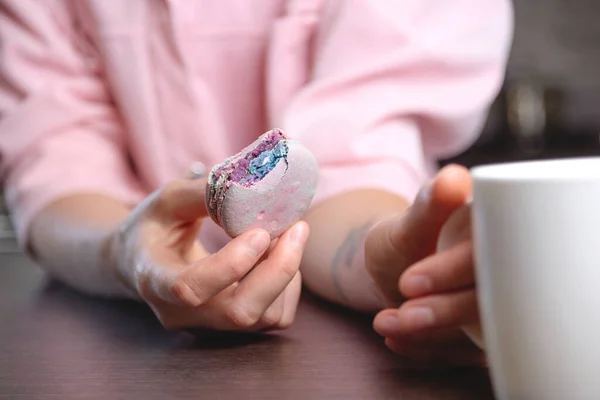 Macaron mordido en la mano de las mujeres junto a la taza de té. Textura de cerca. — Foto de Stock