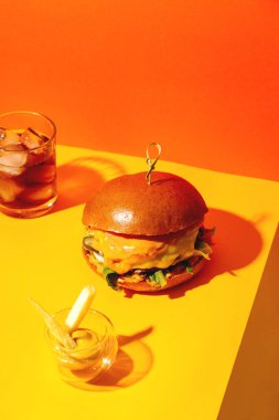 Patates kızartmalı büyük hamburger ve parlak turuncu ve sarı arka planda sos. Amerikan Fast food mutfağı.