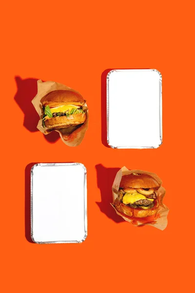 Dos hamburguesas grandes con queso en un paquete sobre un fondo naranja brillante. Entrega de comida rápida. Vista superior. — Foto de Stock