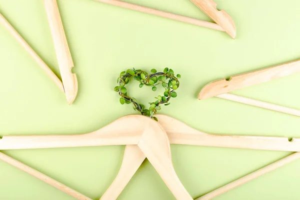 Consumo consapevole concetto di slow fashion. Cuore di appendiabiti intrecciati con pianta su sfondo verde. — Foto Stock