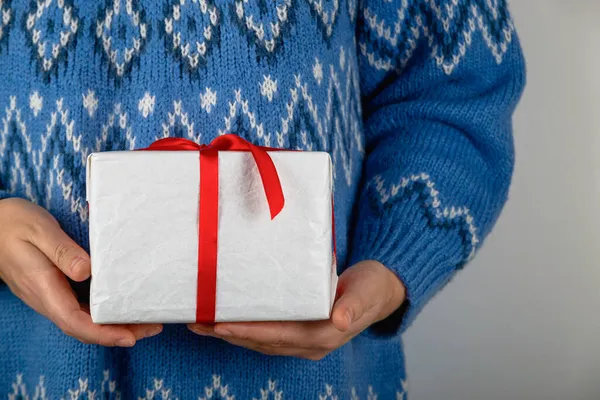 Жінка в синьому светрі тримає білий мінімалістичний різдвяний подарунок — стокове фото