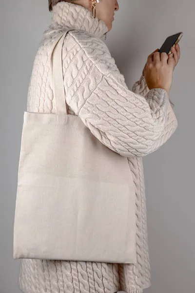Туалетний пакетик накидається на плече жінки в светрі. Макет еко сумки — стокове фото