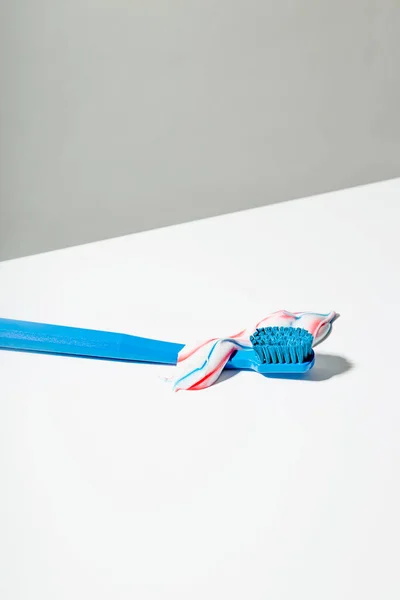 Blue toothbrush with squeezed out red white and blue toothpaste lies on light background — Stock Photo, Image