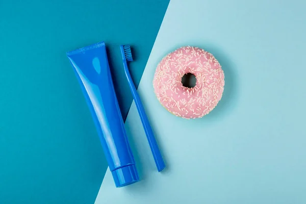 Μπλε σωληνάριο οδοντόκρεμας μπλε οδοντόβουρτσα και ροζ ντόνατ βρίσκονται σε συνδυασμένο μπλε φόντο. Άνω όψη — Φωτογραφία Αρχείου