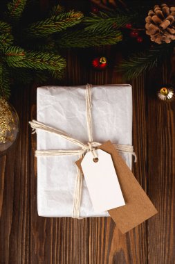 Noel hediyesi etiketi modeli. Ahşap masada küçük beyaz hediye kutusu ve şenlikli süslemeler..