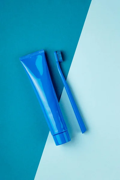 Tube bleu de dentifrice et brosse à dents bleue reposent sur fond bleu combiné. Vue du dessus — Photo