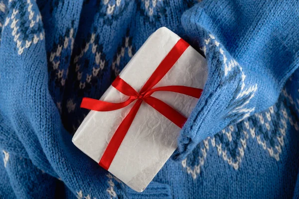 Синій светр, що тримає білий мінімалістичний різдвяний подарунок з червоною стрічкою. Ніхто не лежав . — стокове фото