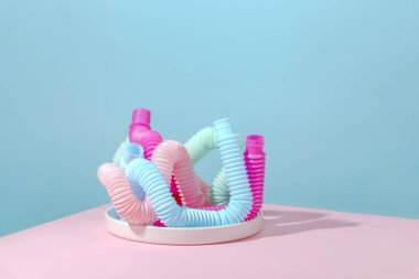 Kıvrımlı pembe, mavi, nane, anti-stres tüpü beyaz tabakta ve pembe arka planda gölgesi var. Akıllı çocuk oyuncağı..