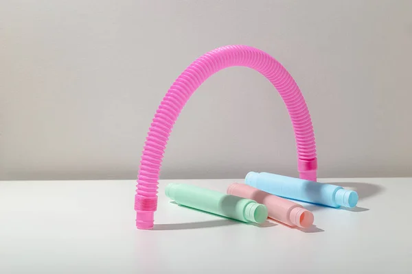 Bleu menthe et rose jouet tube anti-stress pop se trouvent sous tuyau rose vif en forme d'arc avec ombre sur fond clair. Jouet enfant lumineux et pastel — Photo