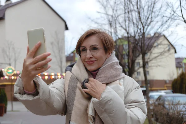 Beautiful baby boomer woman of middle age makes selfie on smartphone on the street. — Photo