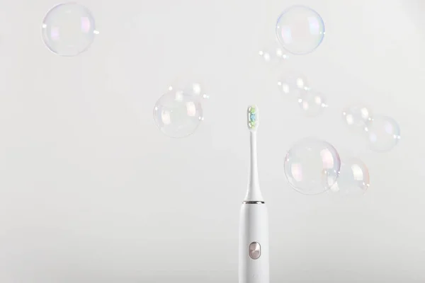 Ηλεκτρονική οδοντόβουρτσα μεταξύ φυσαλίδων σε λευκό φόντο. — Φωτογραφία Αρχείου