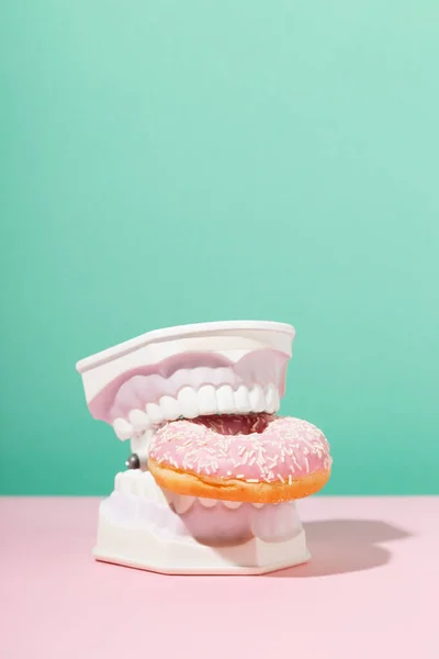 Mâchoires en plastique tenir beignet rose doux dans les dents. Santé dentaire, dentisterie et caries concept. — Photo