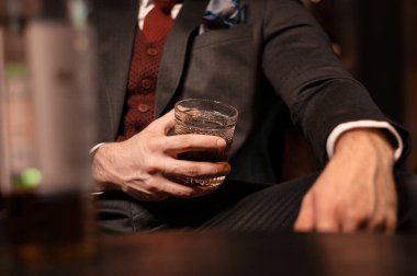 Pahalı takım elbiseli zengin bir adam bir bardak viskiyle karanlık bir odada oturuyor. Bardaktaki alkol. Yakın plan.