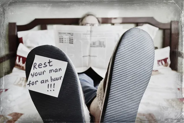 Resting man lying in bed and reading newspaper - fun concept — Stock Photo, Image