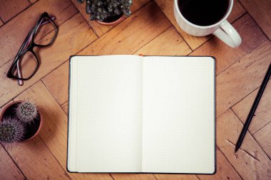 Blank checkered notebook, pencil, glasses, cup of coffee, plants on wooden background, writing concept, top view