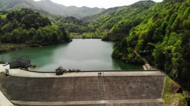 Gökyüzü manzaralı yeşil dağlı bir baraj ve bazı insanlar.