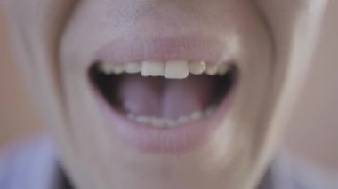 Avrupalı görünümlü, mavi gömlekli, pembe arka planda konuşan ve dudaklarını oynatan beyaz bir adamın Makro yakın çekimi. Yüzün bir kısmı kesilmiş. Yüksek kalite 4k görüntü