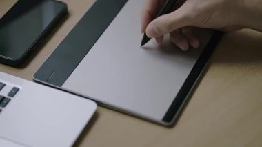  Beyaz bir erkek, çizim tabletine resim çiziyor. Masada telefon ve bilgisayar var. Dolly yana hareket ediyor. Yüksek kalite 4K görüntü..