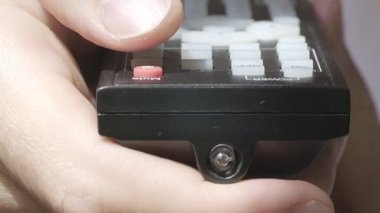 Kafkas bir erkeğin uzaktan kumandayı tutuşu ve kırmızı düğmeye basışı ön planda. Televizyonu açıp evde dinlenme kavramı. Süper makro yüksek kalite 4K görüntü.