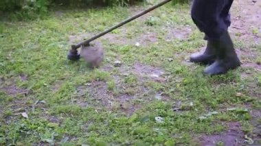 Yazın çimen biçmek için çim biçme makinesi kullanan siyah pantolonlu bir adam. Yüksek kalite 4k görüntü