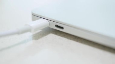 Close-up of pulling laptop by the white usb-c cable connected to the laptop that is sliding on the table. Danger of falling. Steady high quality 4k footage.