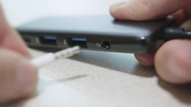 Beyaz erkek eli, onu takarak gri bir usb-c merkezinden kulaklık fişini çekiyor ve çıkarıyor. Yüksek kaliteli 4K görüntüler..