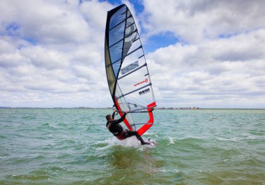 Man riding a windsurfing, huge bright sail, waves, strong wind, adrenaline clipart
