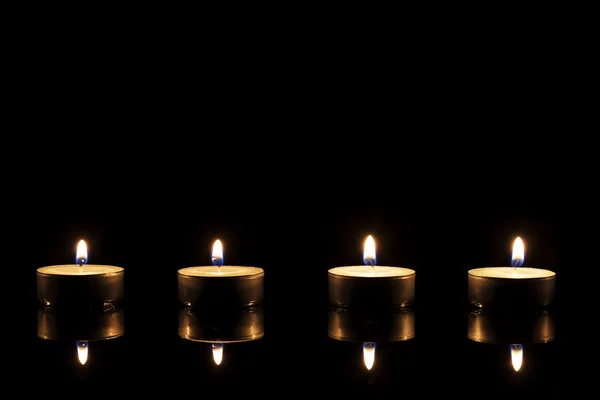 Quatro velas de chá em um espelho preto — Fotografia de Stock