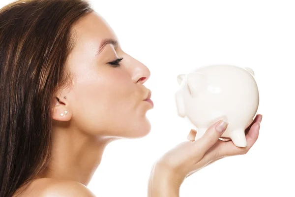 Beautiful brunette woman about to kiss a white piggy bank — Stock Photo, Image